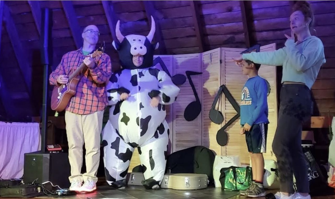Johnny Only performing with an inflatable cow costume during a kids music show